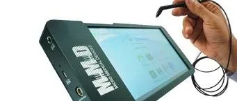 A hand holds a stylus near the screen of an electronic device labeled “MIMIO” with ports and buttons visible on its side. The device appears to be a touchscreen or writing pad.