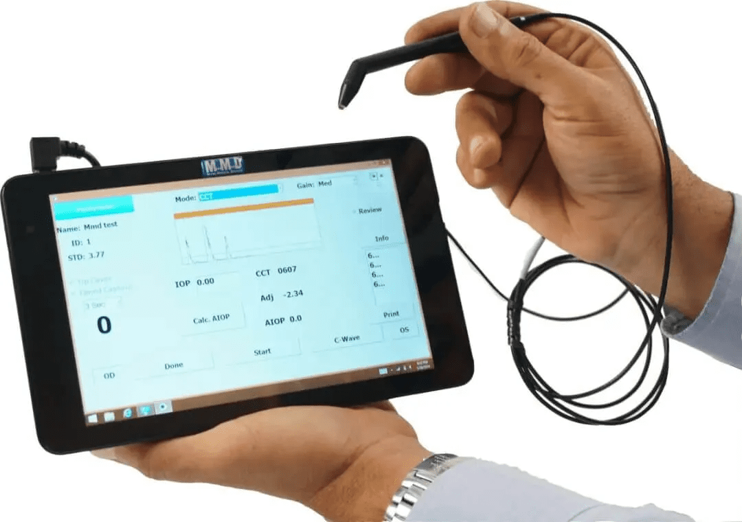 A person holds a touchscreen tablet displaying a measurement interface, using a wired stylus attached to the device, suggesting data input or diagnostic testing.