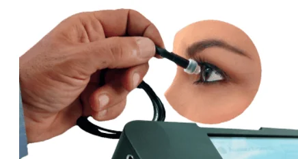 A hand holds a medical instrument close to a womans eye, with the device connected by a cable, suggesting an eye examination or diagnostic procedure.