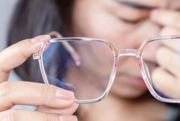 A woman experiencing eye strain while holding eyeglasses.